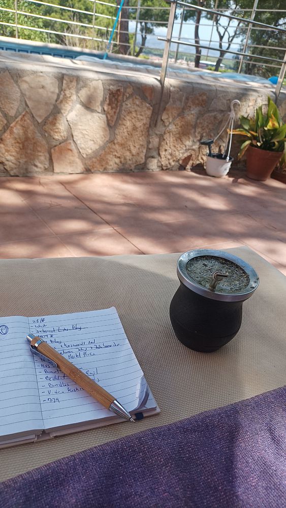 A cozy outdoor workspace featuring a notebook, a pen, and a traditional mate cup.