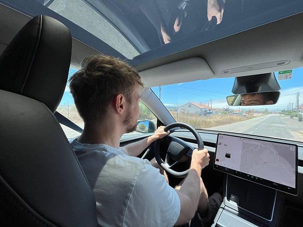 A person is driving a car on a wide road with a digital display showing navigation.