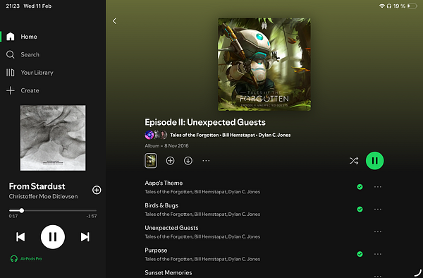 Photograph of a man focusing on writing in a notebook with a laptop and smartphone on a table, in a stylish room with wood paneling and modern decor.