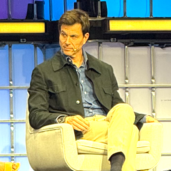 Toto Wolff is seated on a stage, engaged in an interview, displaying a thoughtful expression.