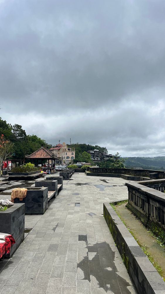 A scenic view of a plaza in Kintamani with cloudy skies and surrounding greenery.