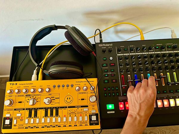 A hand is adjusting controls on a music production setup featuring a yellow synthesizer and a black drum machine.