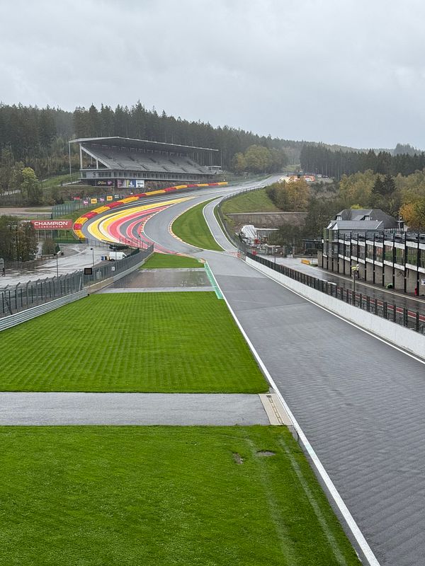 Wet Circuit de Spa-Francorchamps racing track with colorful curbs and empty grandstands on a cloudy day.