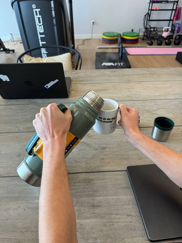 A person is pouring from a thermos into a coffee mug in a coworking space.