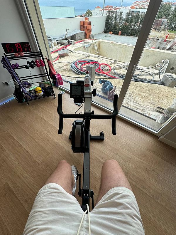 A person is seated on a rowing machine with a view of a construction site outside.