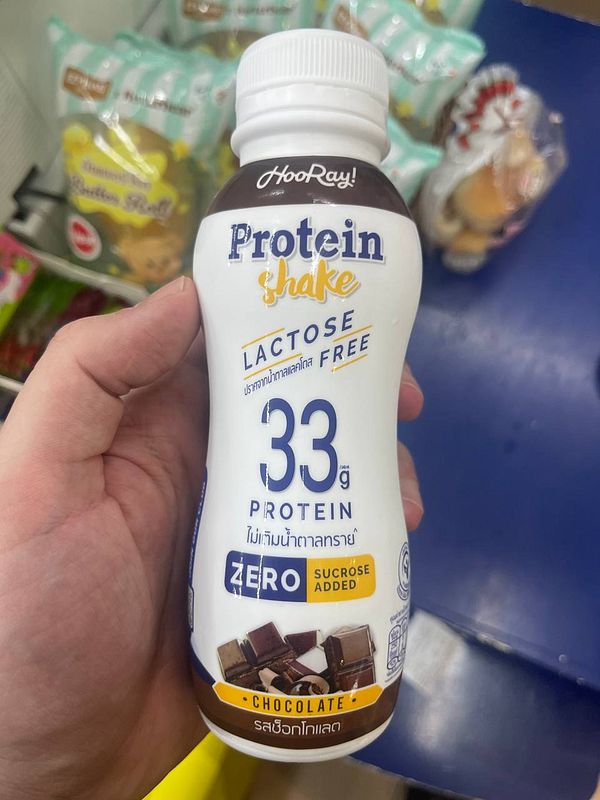 A hand holds a chocolate-flavored protein shake bottle labeled as lactose-free with high protein content.