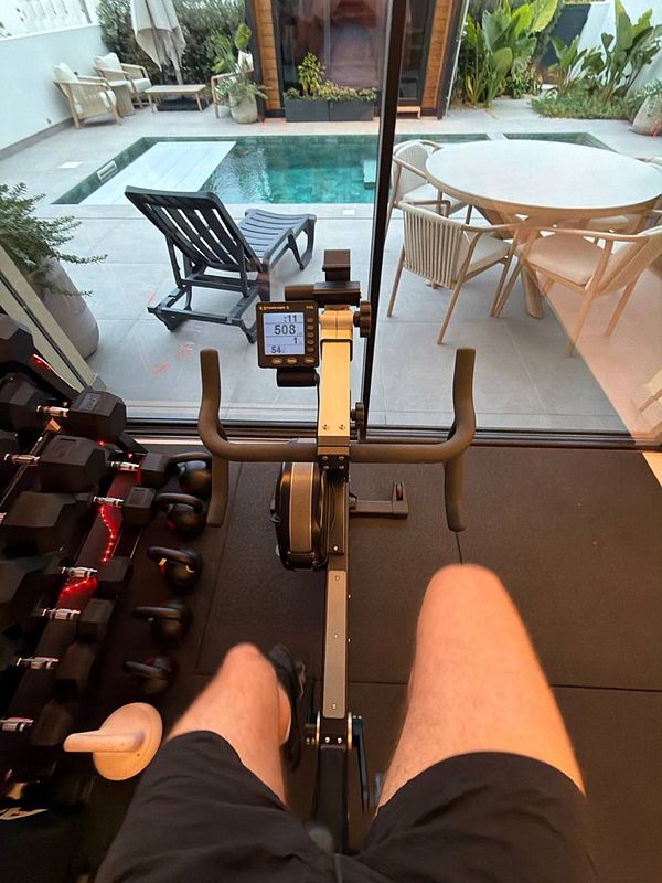 Indoor exercise bike setup facing a patio with a pool, outdoor lounge chairs, and a dining table.