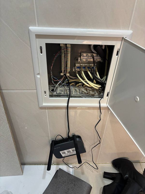 A patch box is open with various cables inside, and a Wi-Fi router is connected outside the box.