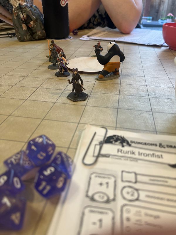 A tabletop scene from a Dungeons & Dragons game featuring miniatures, dice, and character sheets.