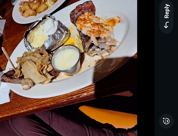A delicious plate featuring steak, lobster, a baked potato, and sautéed vegetables.