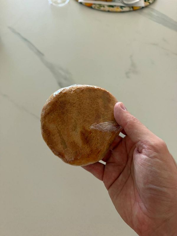 Close-up image of a hand holding a golden brown, flaky croissant against a blurred background.