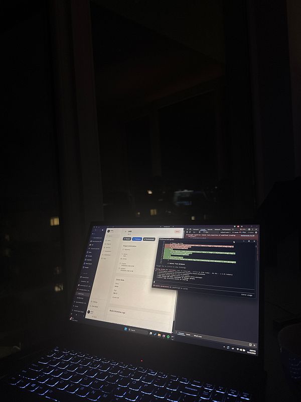 A laptop screen displays a coding environment in a dimly lit room.