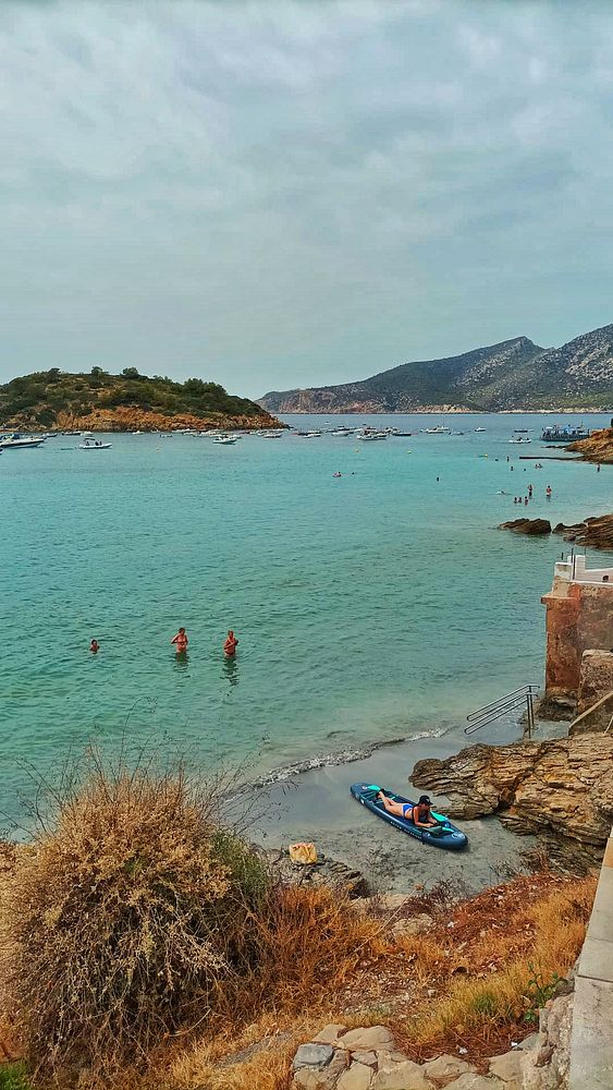 A scenic beach view on a cloudy Sunday with people enjoying the water.