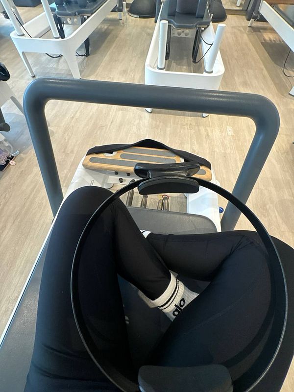 A person is seated on a Pilates reformer, preparing for a workout.