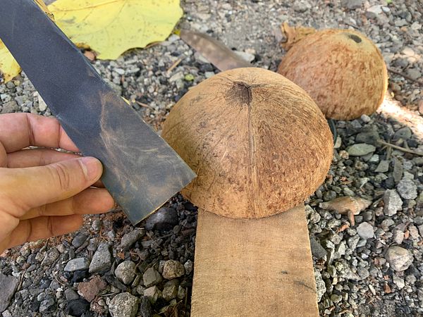 A handmade coconut shell bowl with an uneven cut and a natural, rustic look, resting on a textured fabric surface.