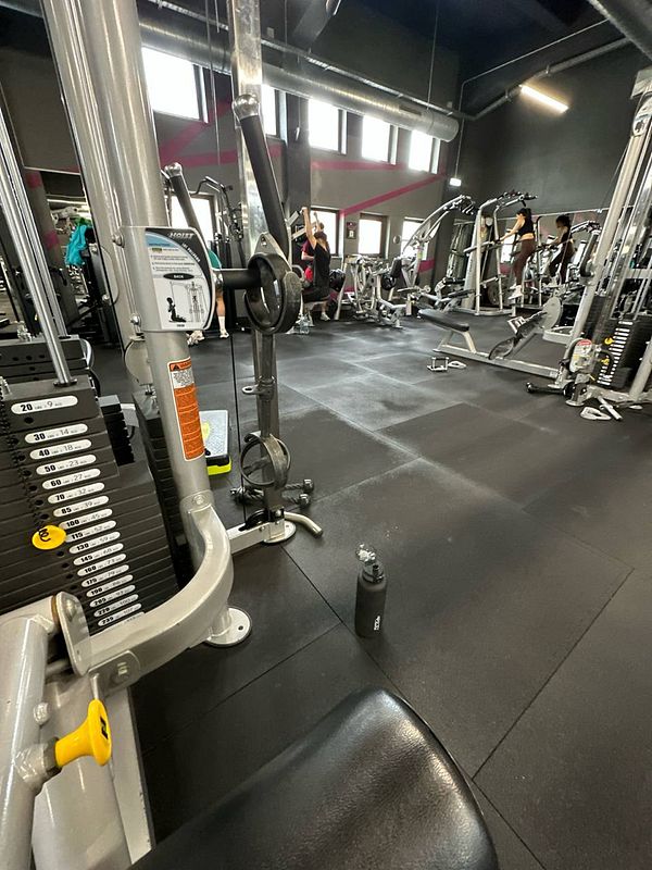 The image captures a gym interior with various exercise equipment and individuals working out.