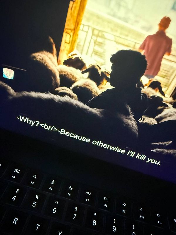 A scene from a film featuring a child in a dimly lit room surrounded by sheep, with subtitles displaying a threatening dialogue.