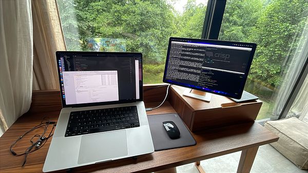 A modern workspace featuring a laptop and an external monitor with a view of greenery outside.