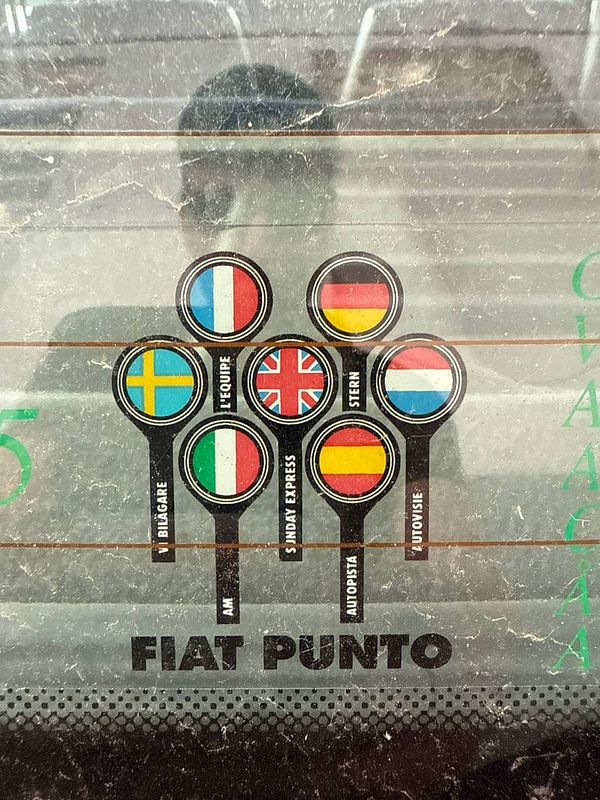 The image features a collection of country flags and text related to driving regulations on a car's rear window.