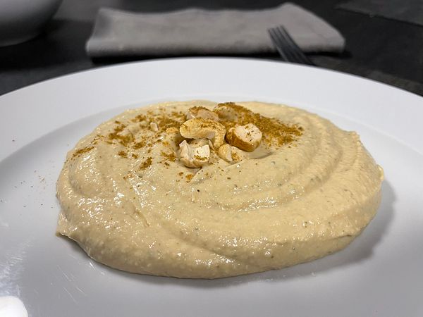 A plate of hummus garnished with nuts and spices.