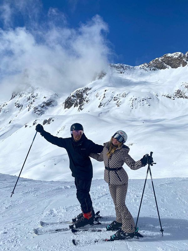 A couple enjoys skiing on a snowy mountain slope under a clear blue sky.