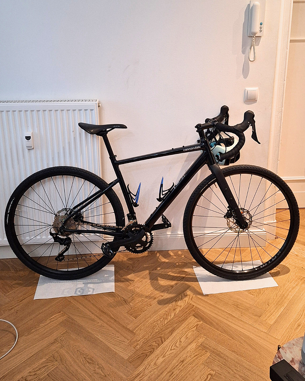 A black gravel bike is positioned indoors next to a wall.