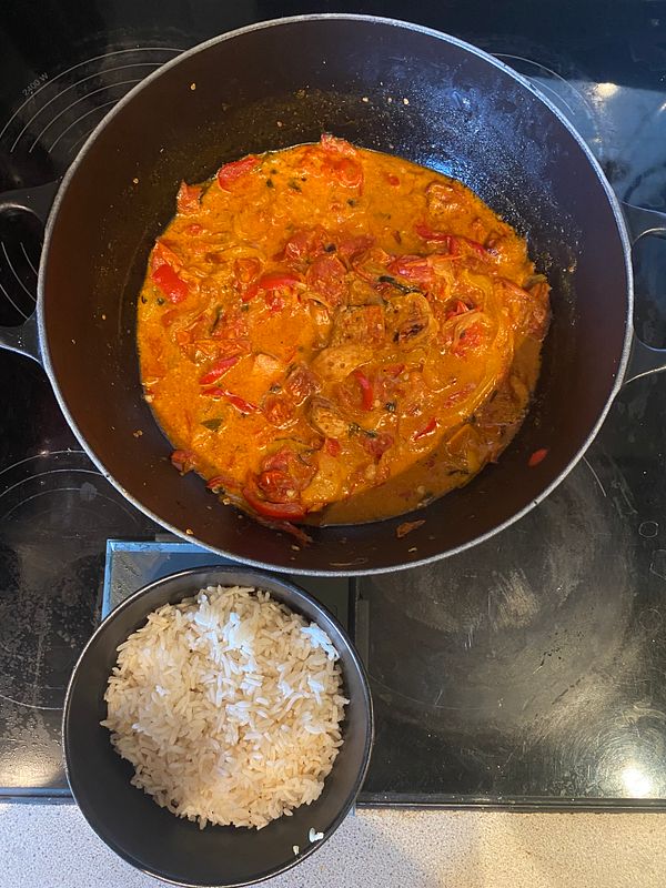 Close-up of a black bowl filled with a curry dish featuring vegetables and chicken pieces.