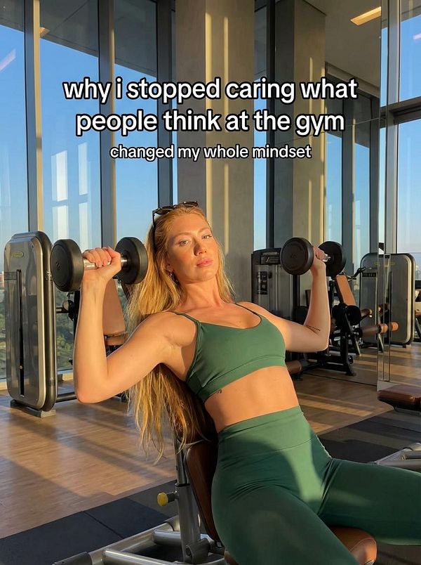 A woman is exercising in a gym, lifting dumbbells while showcasing a confident mindset.