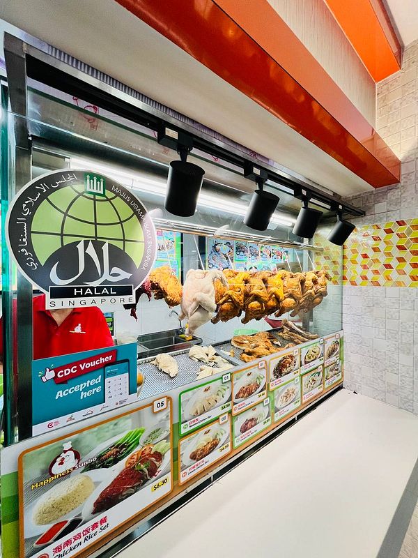 A food stall displaying various chicken rice dishes and a selection of halal options.