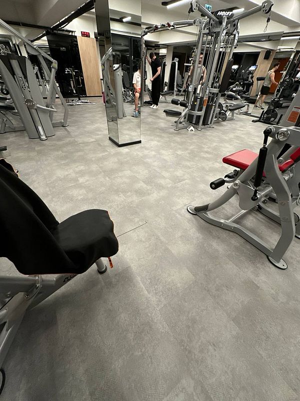 A gym interior featuring various workout equipment and two individuals engaged in conversation.