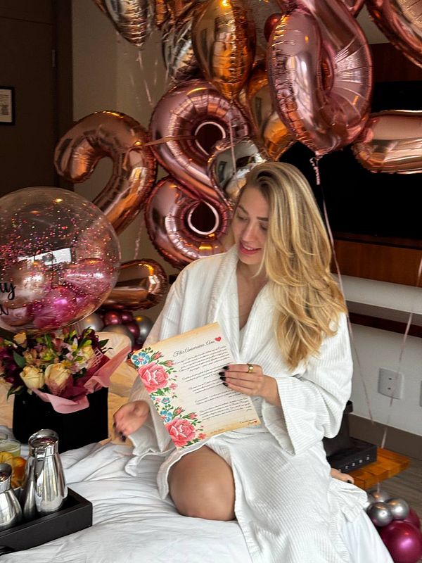 A woman in a white robe enjoys a birthday surprise surrounded by balloons and a floral menu.