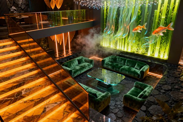 Futuristic living room with emerald green velvet sofas arranged around a clear glass coffee table etched with topographic lines. Behind, a luminous feature wall of vertical green acrylic tubes and translucent wave panels displays oversized koi, with wisps of fog pooling at the base; overhead, a constellation of tiny LEDs sparkles, while backlit amber onyx stairs, a smoked-glass balustrade, and black slate flooring outlined by linear lighting complete the neon green and warm orange ambiance.