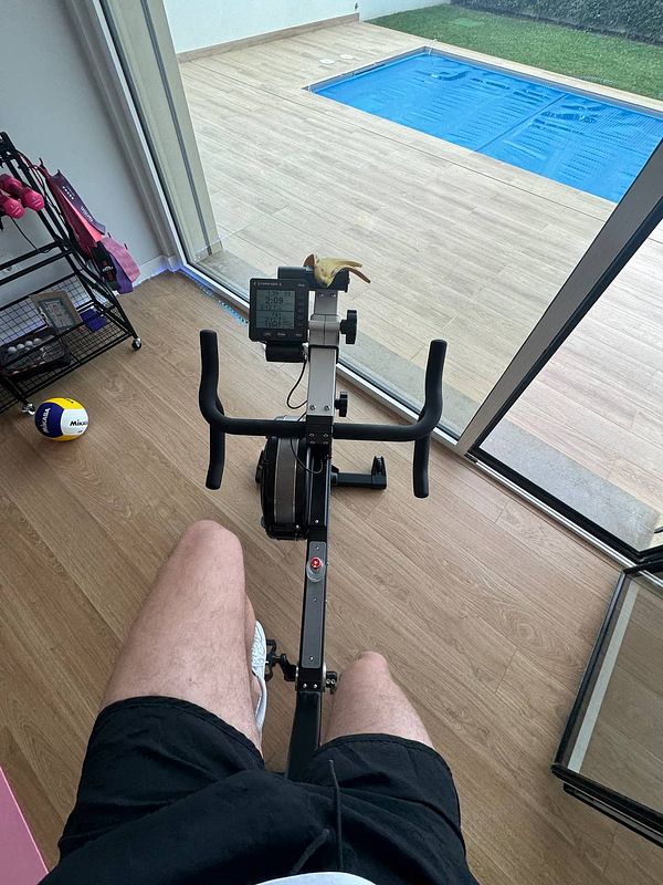 A person is using a rowing machine in a home gym with a view of a swimming pool.