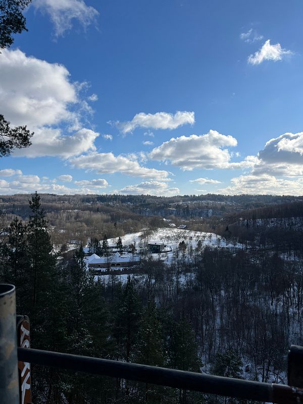 A scenic winter landscape featuring rolling hills, snow-covered ground, and a bright blue sky with fluffy clouds.