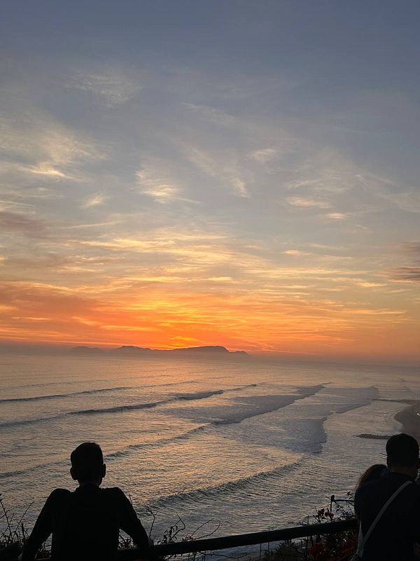 A vibrant sunset over a coastal town with buildings and the Pacific Ocean in the background.