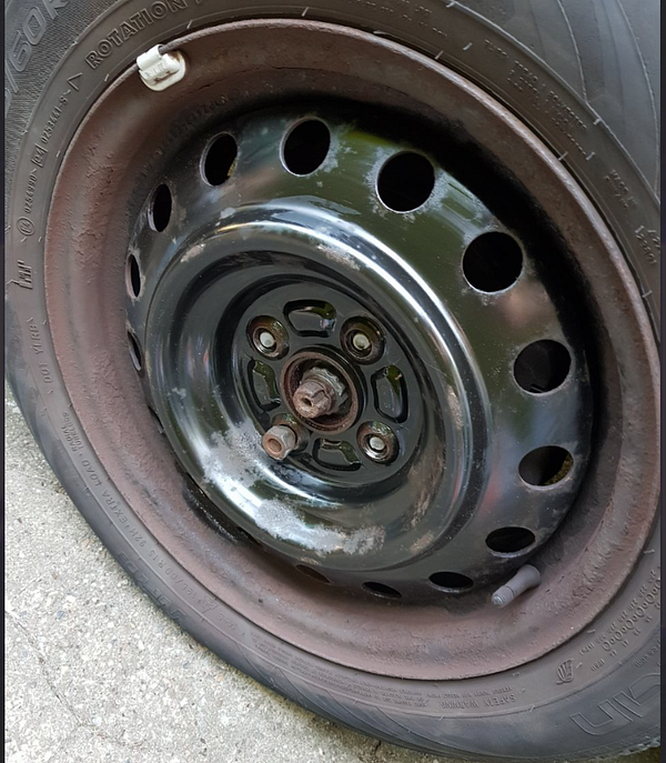 A close-up view of a car wheel with a missing stud and a partially rusted rim.