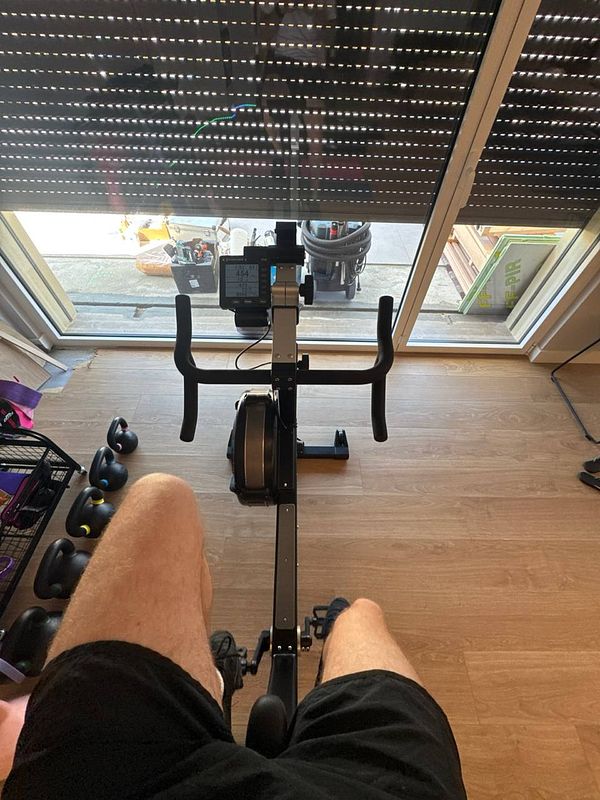 A person is seated on a rowing machine, preparing for a workout at home.