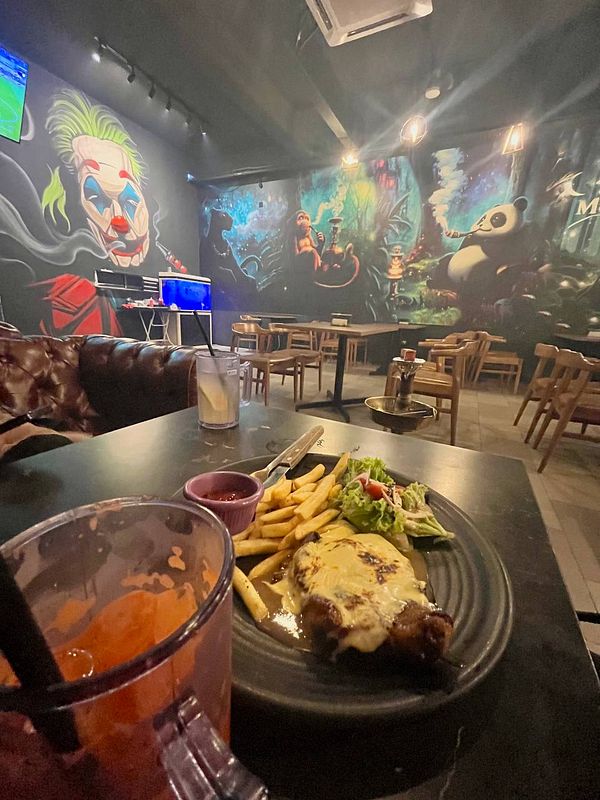 A dining scene featuring a plate of chicken chop, fries, and carrot juice in a vibrant, artistically decorated restaurant.