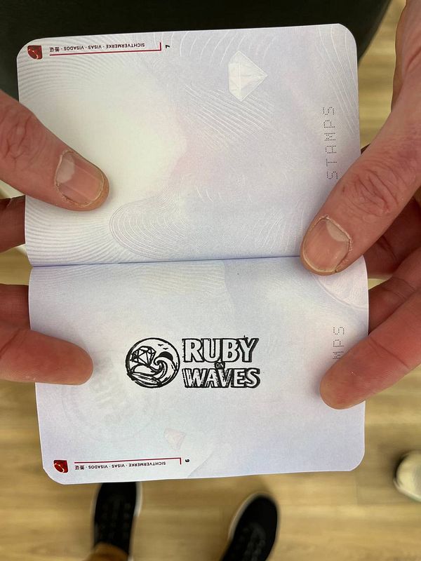 A red rubber stamp with the Ruby on Waves logo and an impression of the logo stamped on paper.