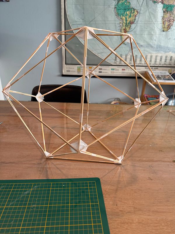 A handcrafted icosahedron composed of twenty equilateral triangle faces displayed on a wooden surface.