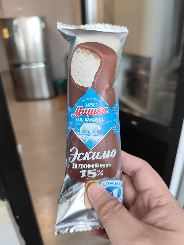 A hand holds a chocolate-covered ice cream bar in a kitchen setting.