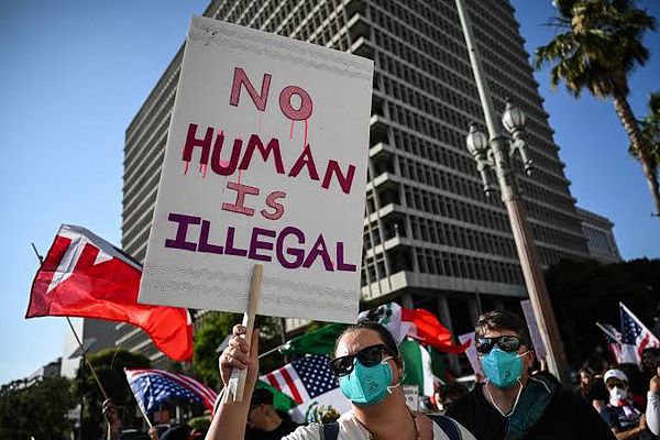 A protest scene featuring individuals holding a sign advocating for immigrant rights.