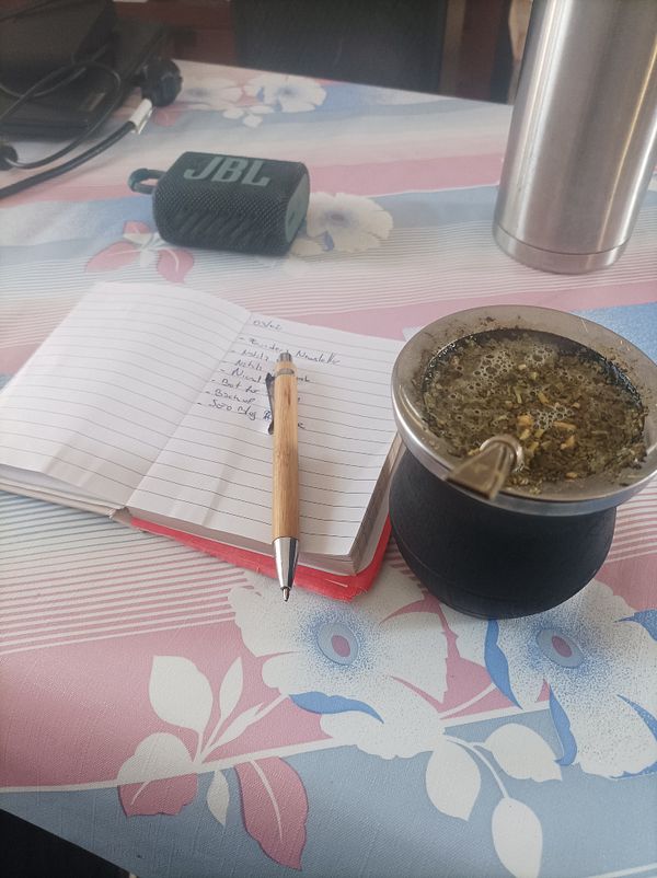 A workspace featuring a notebook, a pen, a mate cup, and a portable speaker.