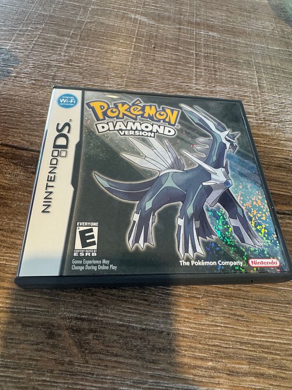 Hand holding the Pokémon Diamond video game case for Nintendo DS against a wiring background.
