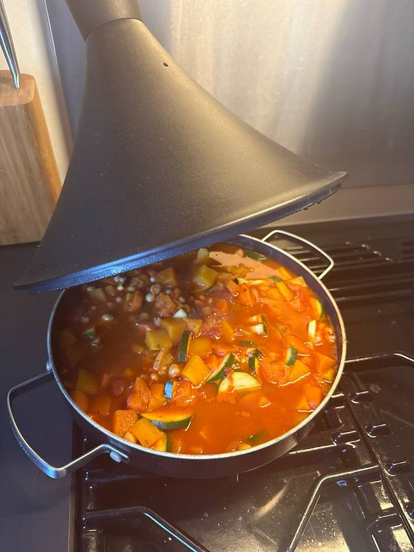 A tajine pot filled with a colorful vegetable stew is shown on a stovetop.