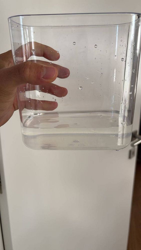 A hand holds a clear container filled with water droplets.