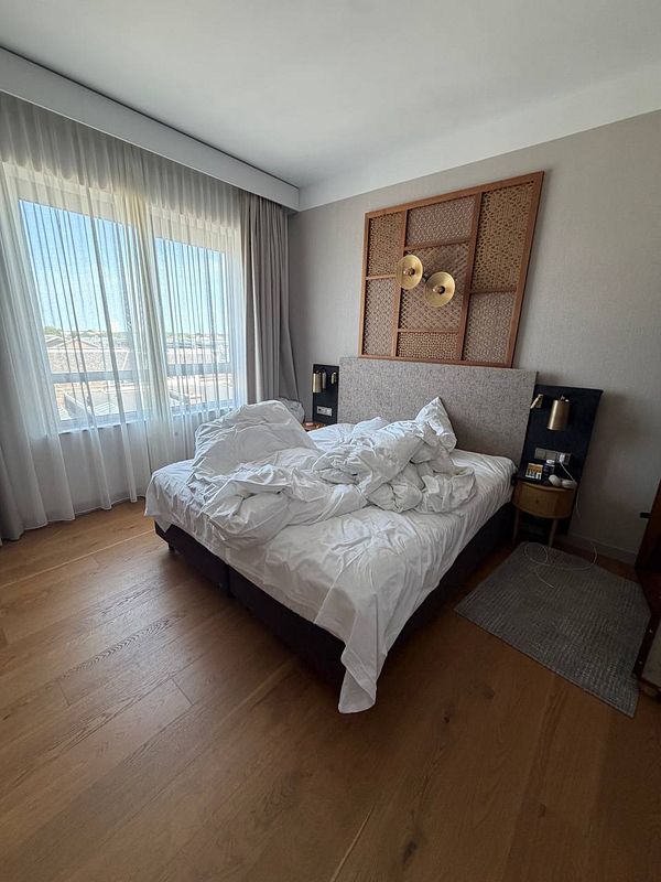 Photo of a hotel room bed with disheveled sheets and a person lying down with a phone.