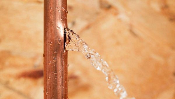 Water is spraying from a drilled copper pipe, creating a wet floor situation.