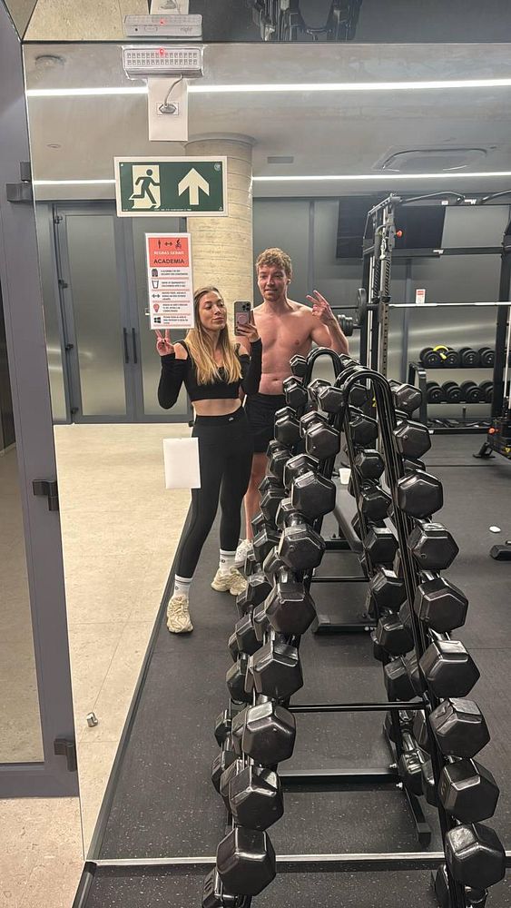 A gym selfie featuring two individuals in a modern fitness center.