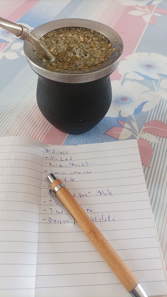 A cozy indoor scene with a mate gourd and bombilla on a wooden table, alongside various task-related items including a planner and colorful sticky notes.